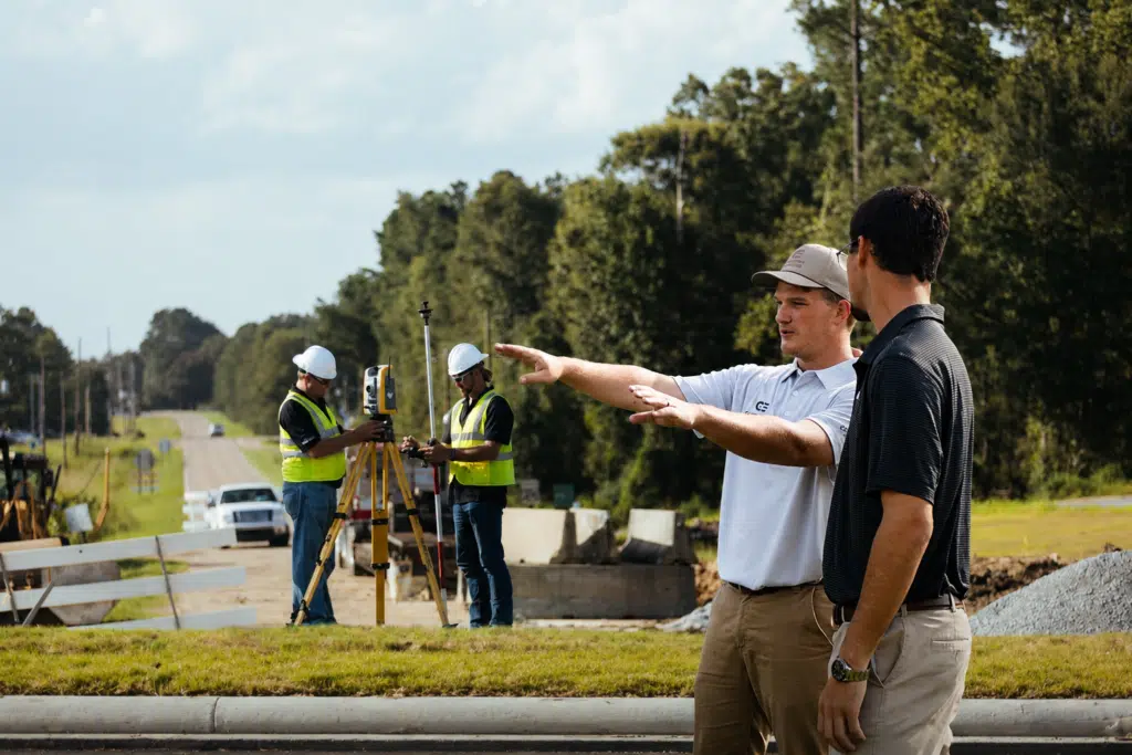 Two men in vests surveying and two men talking.